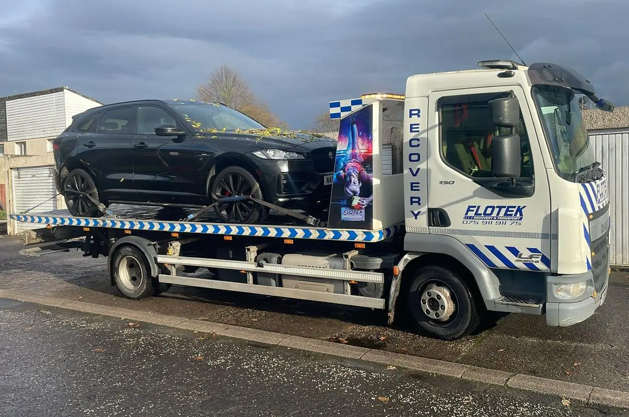 Flotek recovery truck transporting a black Jaguar SUV